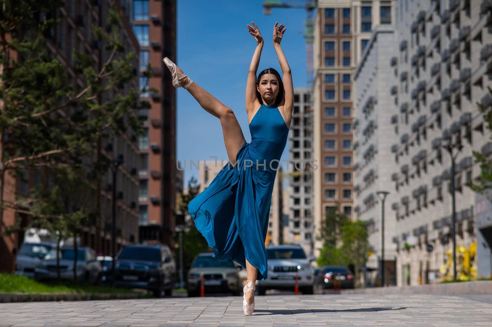Beautiful Asian ballerina in blue dress posing in splits outdoors. Urban landscape. by mrwed54