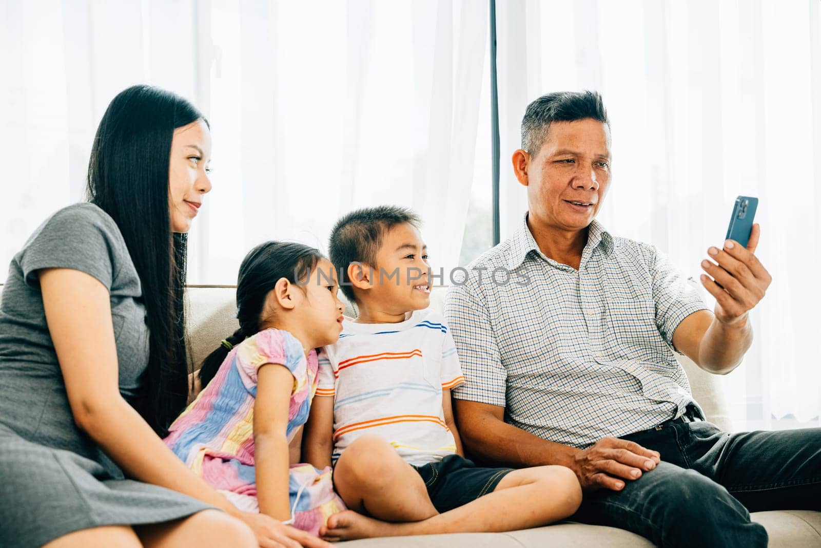 A cheerful family enjoys entertainment on a smartphone laughing together on a couch. This portrays familial happiness bonding and shared moments of technology entertainment.