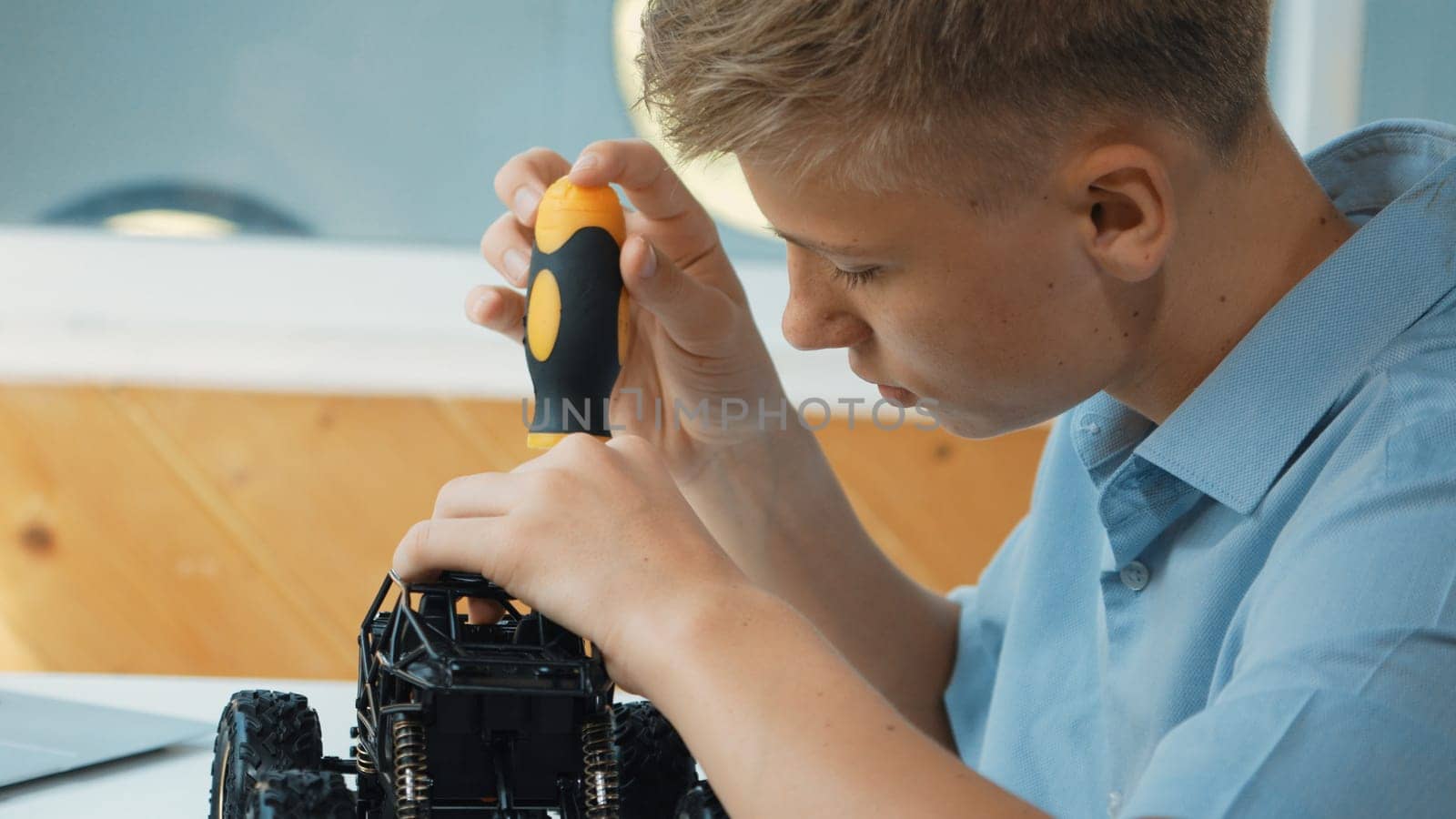 Close up of young student tighten the nut by using screwdriver. Caucasian teenager repairing or fixing car model while inspect robotic machine construction at STEM technology class. Edification.