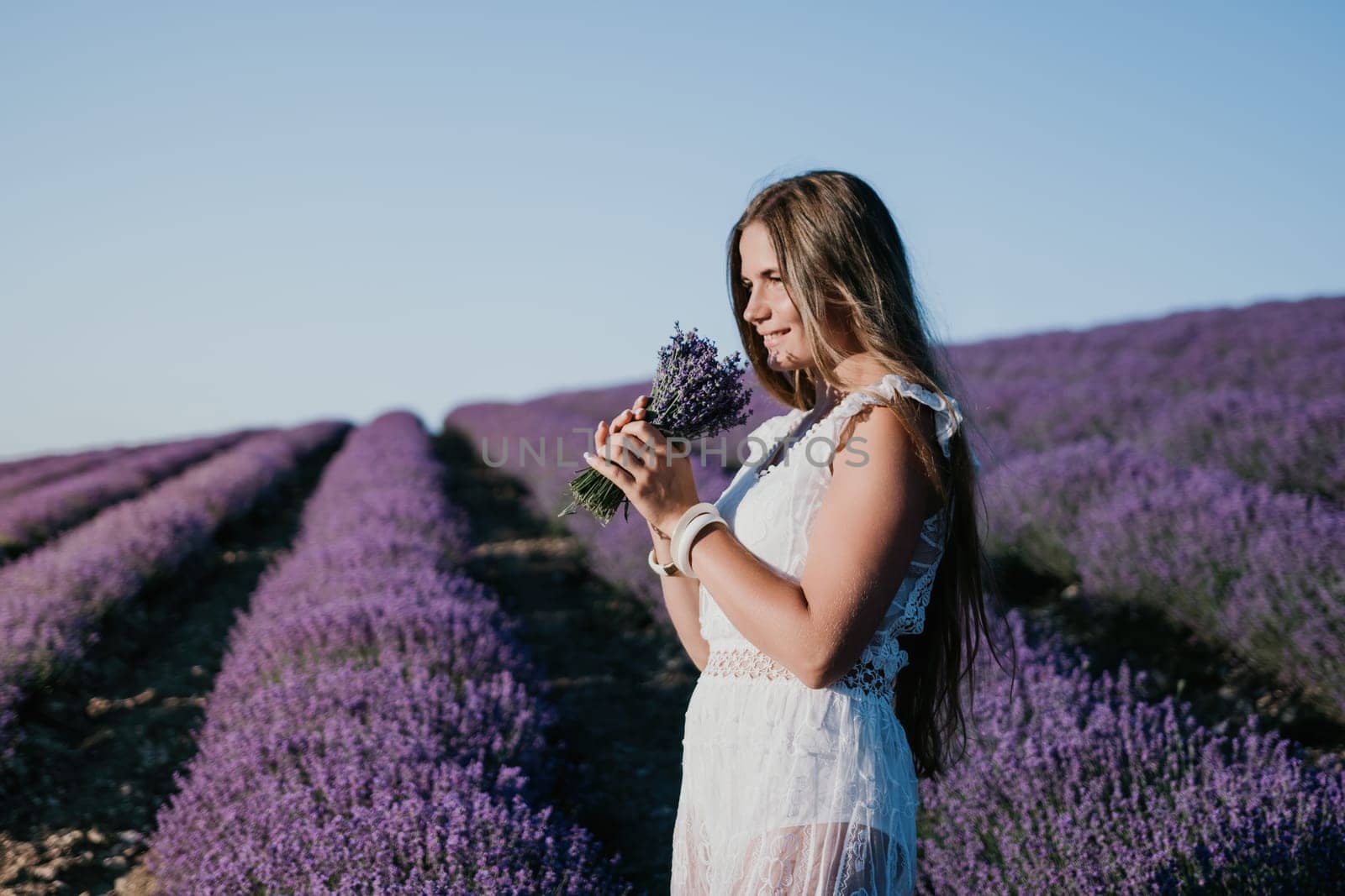 Woman lavender field. Happy carefree woman in a white dress walking in a lavender field and smelling a lavender bouquet on sunset. Ideal for warm and inspirational concepts in wanderlust and travel. by panophotograph