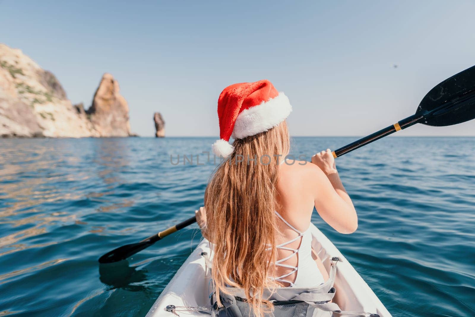 Woman in kayak back view. Happy young woman with long hair floating in transparent kayak on the crystal clear sea. Summer holiday vacation and cheerful female people relaxing having fun on the boat