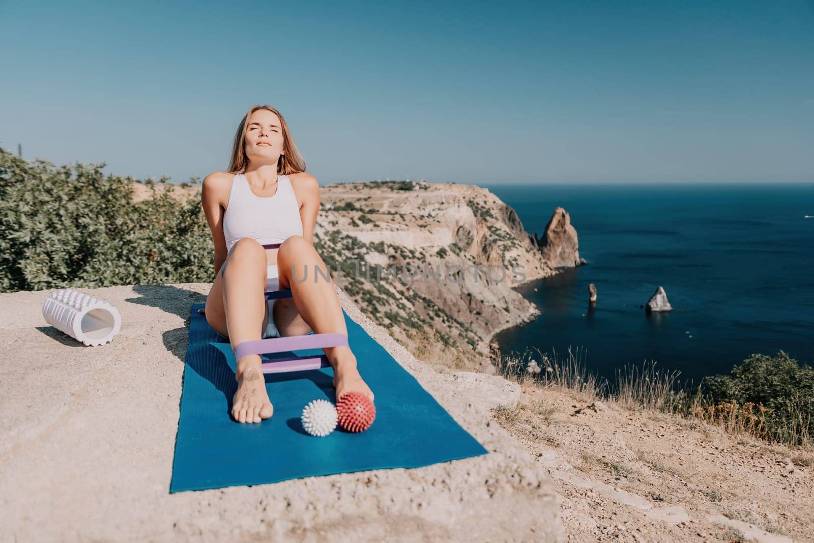 Woman sea pilates. Sporty happy middle aged woman practicing fitness on yoga mat using rubber tape, massage balls, and rollers near sea, smiling active female outside, enjoying healthy lifestyle by panophotograph
