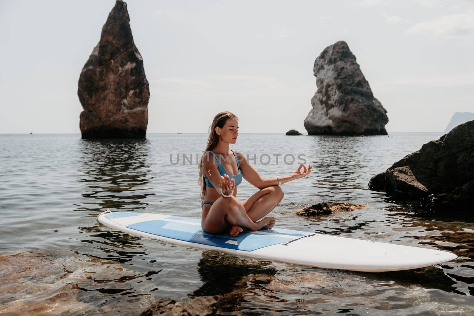 Woman sup yoga. Happy sporty woman practising yoga pilates on paddle sup surfboard. Female stretching doing workout on sea water. Modern individual female hipster outdoor summer sport activity. by panophotograph