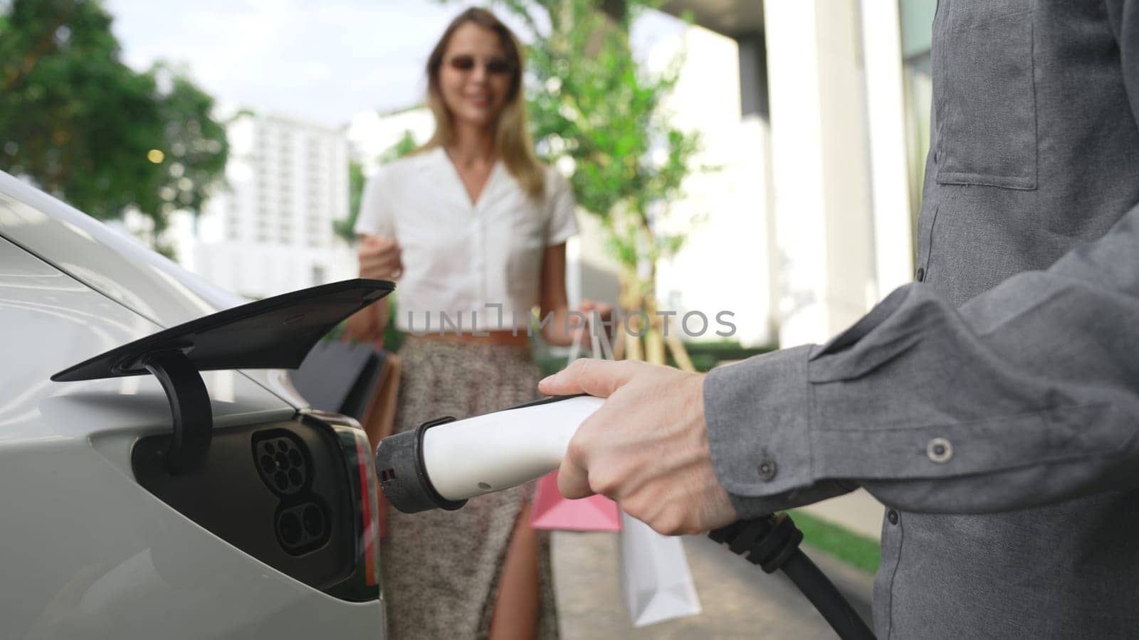 Young couple travel with EV electric car charging at green sustainable home in summer shows urban sustainability lifestyle by green clean rechargeable energy of electric vehicle innards