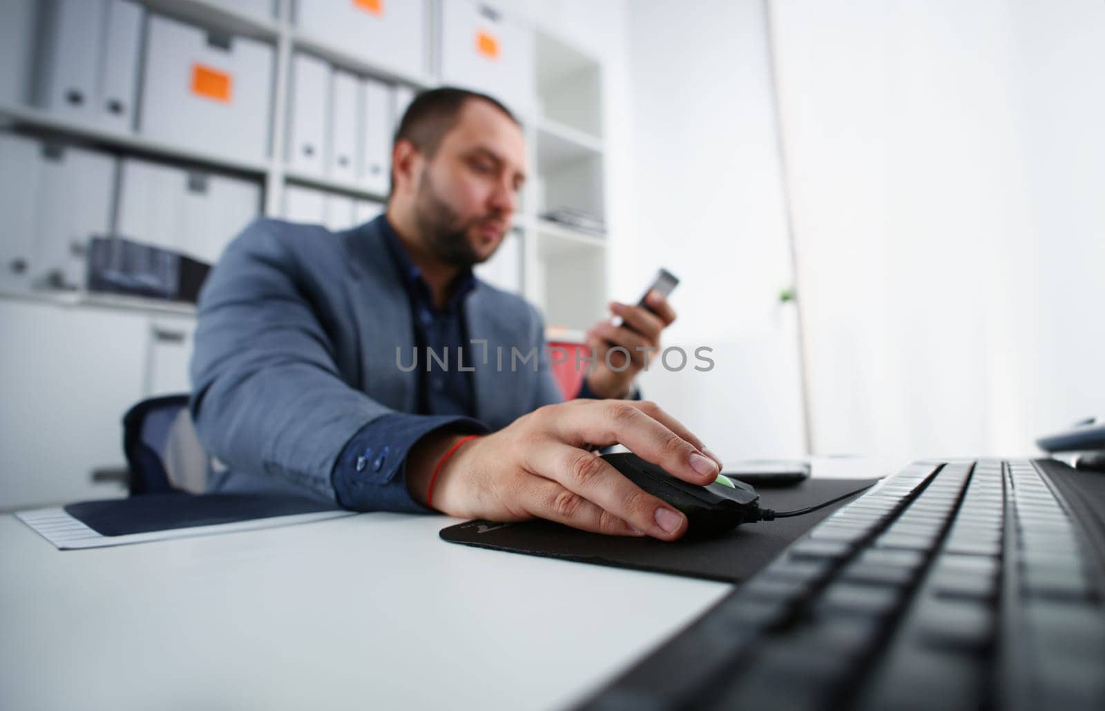 businessman work on computer hold mouse in arm and mobile phone in other closeup office worker concept