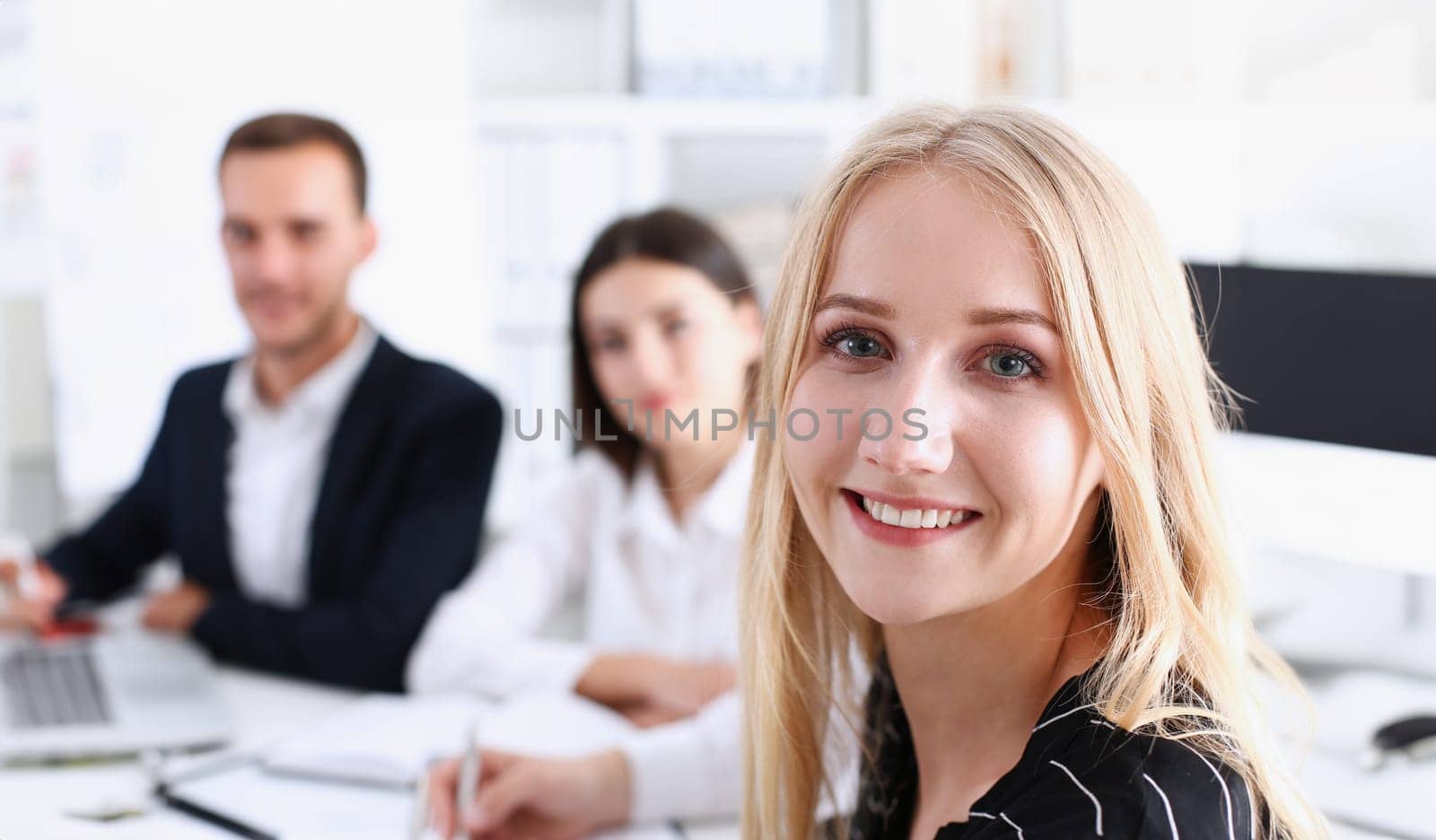 Beautiful smiling cheerful girl at workplace look in camera with colleagues group in background. White collar worker at workspace job offer modern lifestyle client visit profession train concept