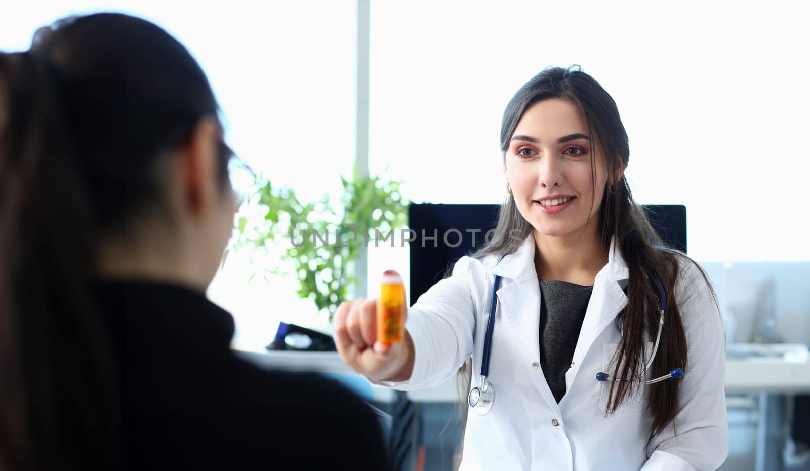 Female medicine doctor hand hold jar of pills and write prescription to patient at worktable. Panacea and life save prescribing treatment legal drug store concept.