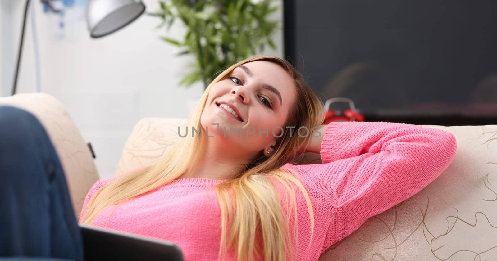 young beautiful blond woman lie on the sofa in livingroom hold tablet in arms sunny morning concept