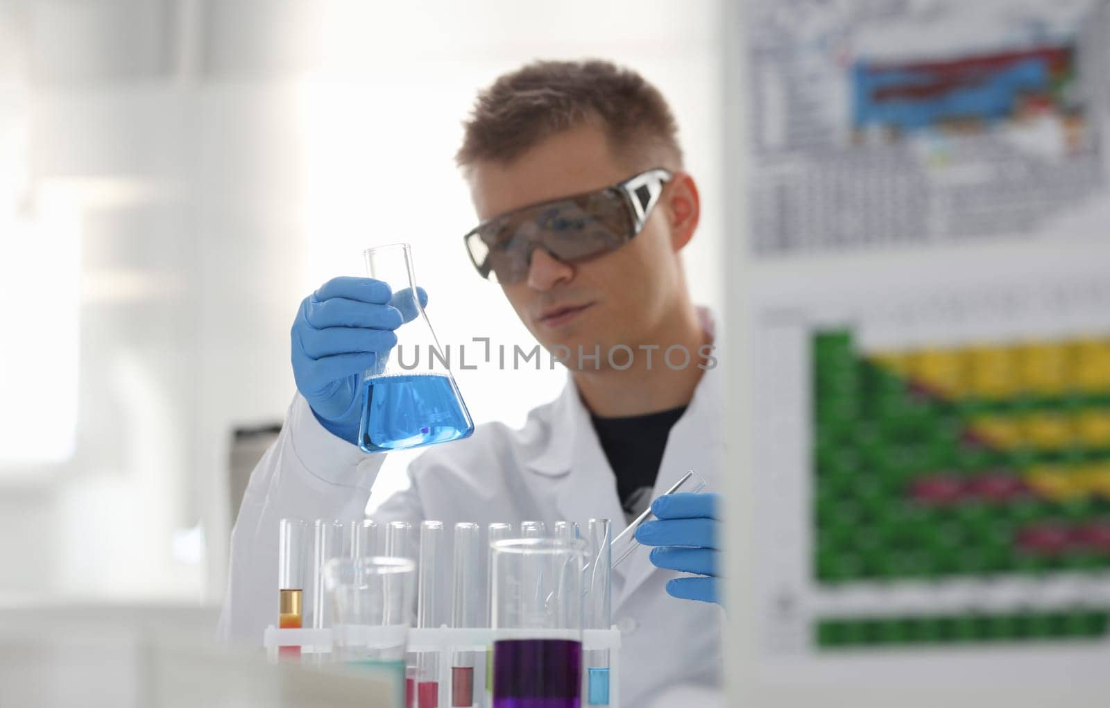 A male chemist holds test tube of glass in his hand overflows a liquid solution of potassium permanganate conducts an analysis reaction takes various versions of reagents using chemical manufacturing.