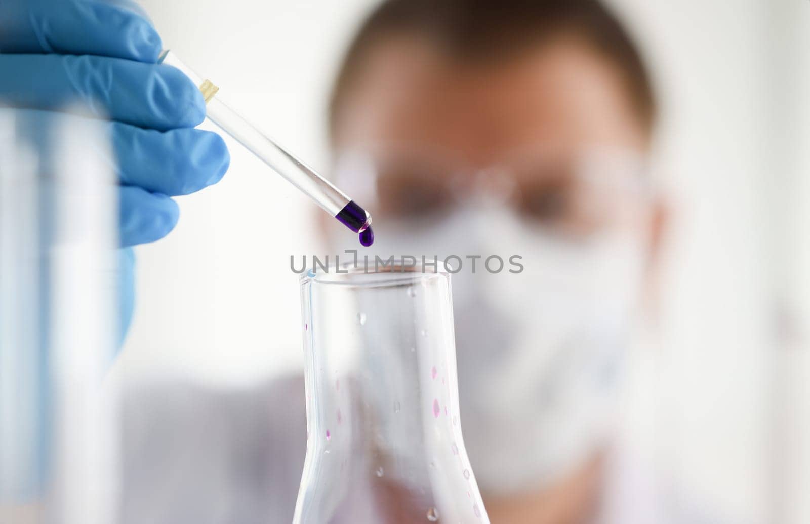 A male chemist holds test tube of glass in his hand overflows a liquid solution of potassium permanganate conducts an analysis of water samples versions of reagents using chemical manufacturing.