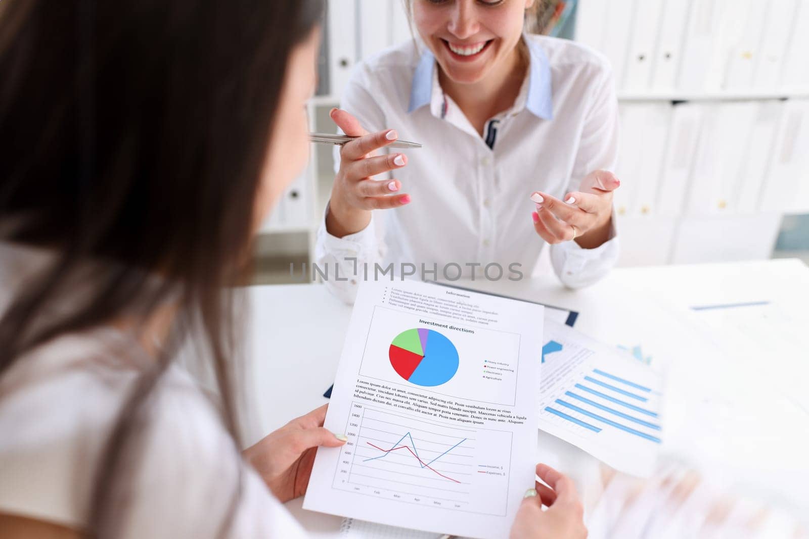 Businesswoman holding a silvery pen in her hand indicates the interlocutor for a digram on the form of annual report on the financing of organizations trains the processing of this statistical study.