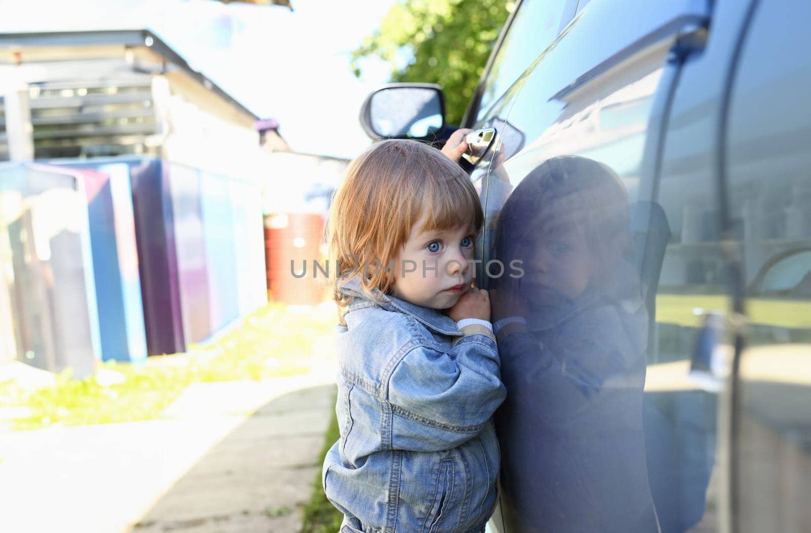 Little fashion child holds the car handle in a jeans jacket smiles and looks into the camera suitable for a fashion store