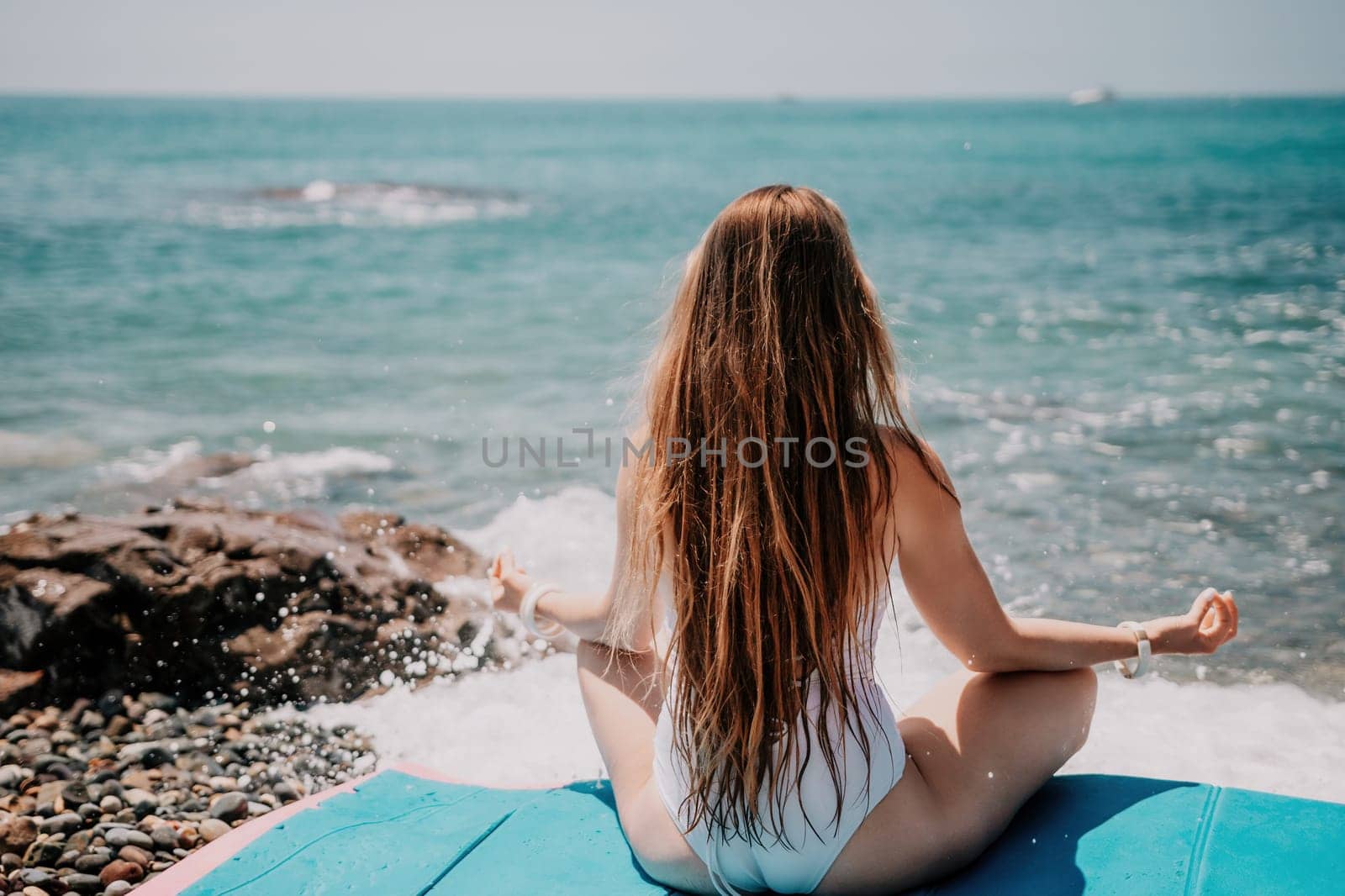 Woman yoga sea. Young woman with long hair in white swimsuit and boho style braclets practicing outdoors on yoga mat by the ocean on sunny day. Women's yoga fitness routine. Healthy lifestyle, harmony by panophotograph