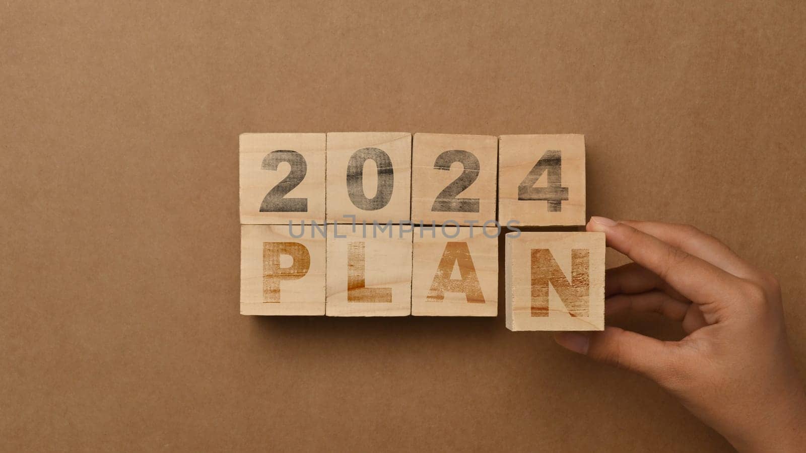 Hand arranging wooden blocks with 2024 PLAN word on brown background. Business plan, goals and strategy concept.