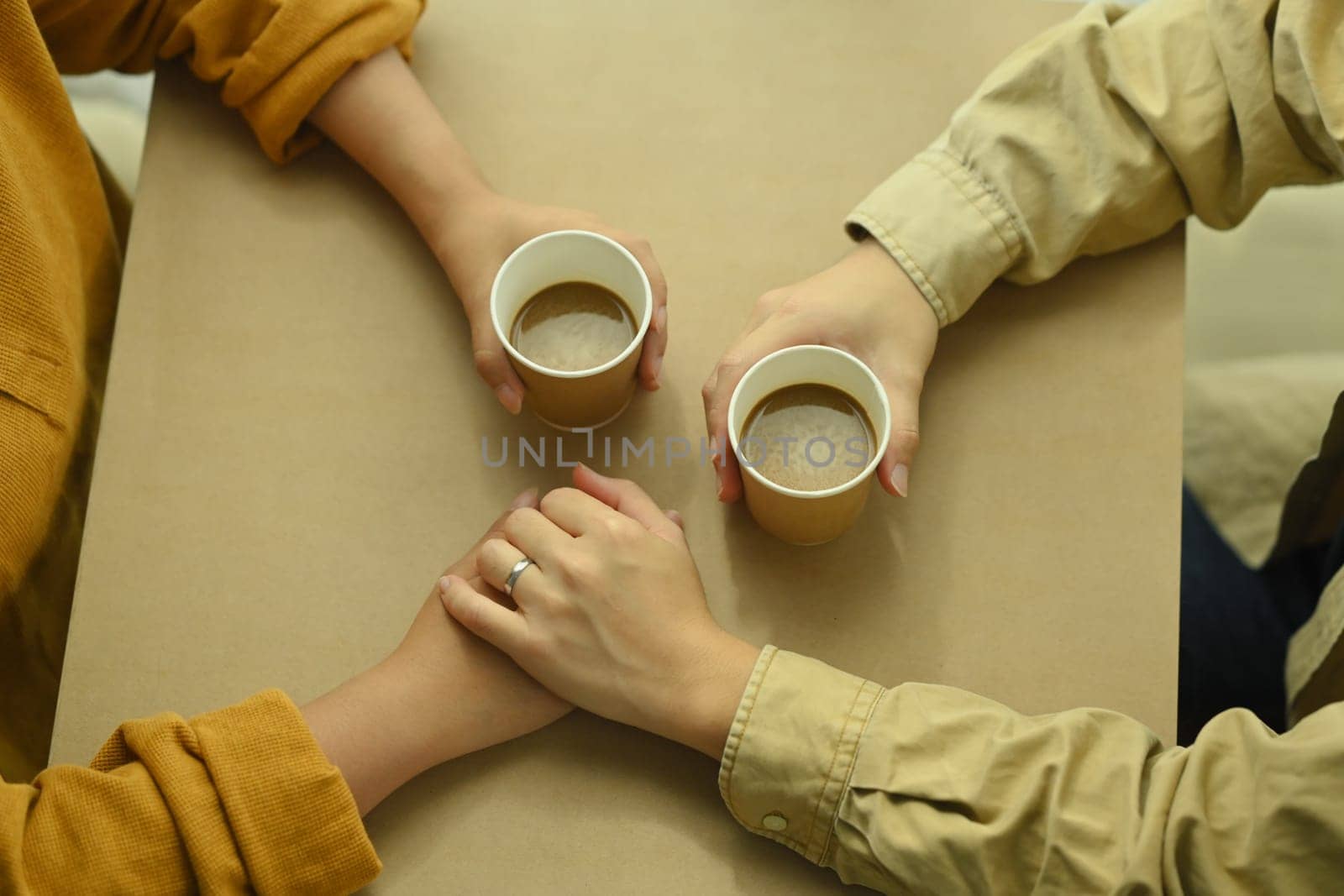 Loving young couple holding hands on table with coffee cups. Love, relationship and lifestyle concept by prathanchorruangsak