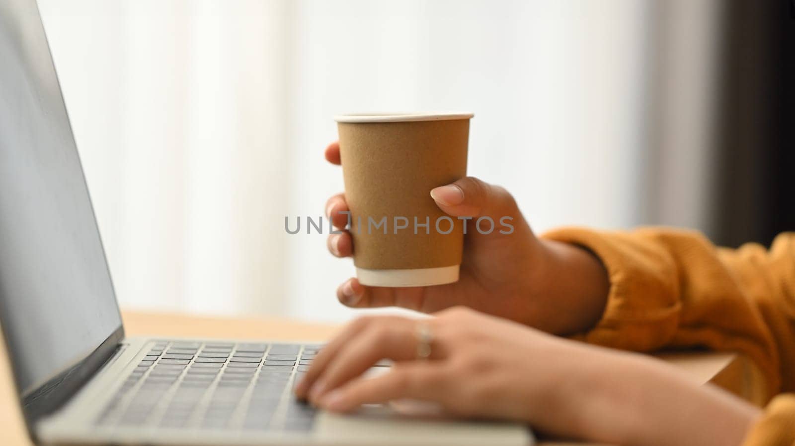 Side view of woman hand holding paper up of coffee and typing on laptop computer by prathanchorruangsak