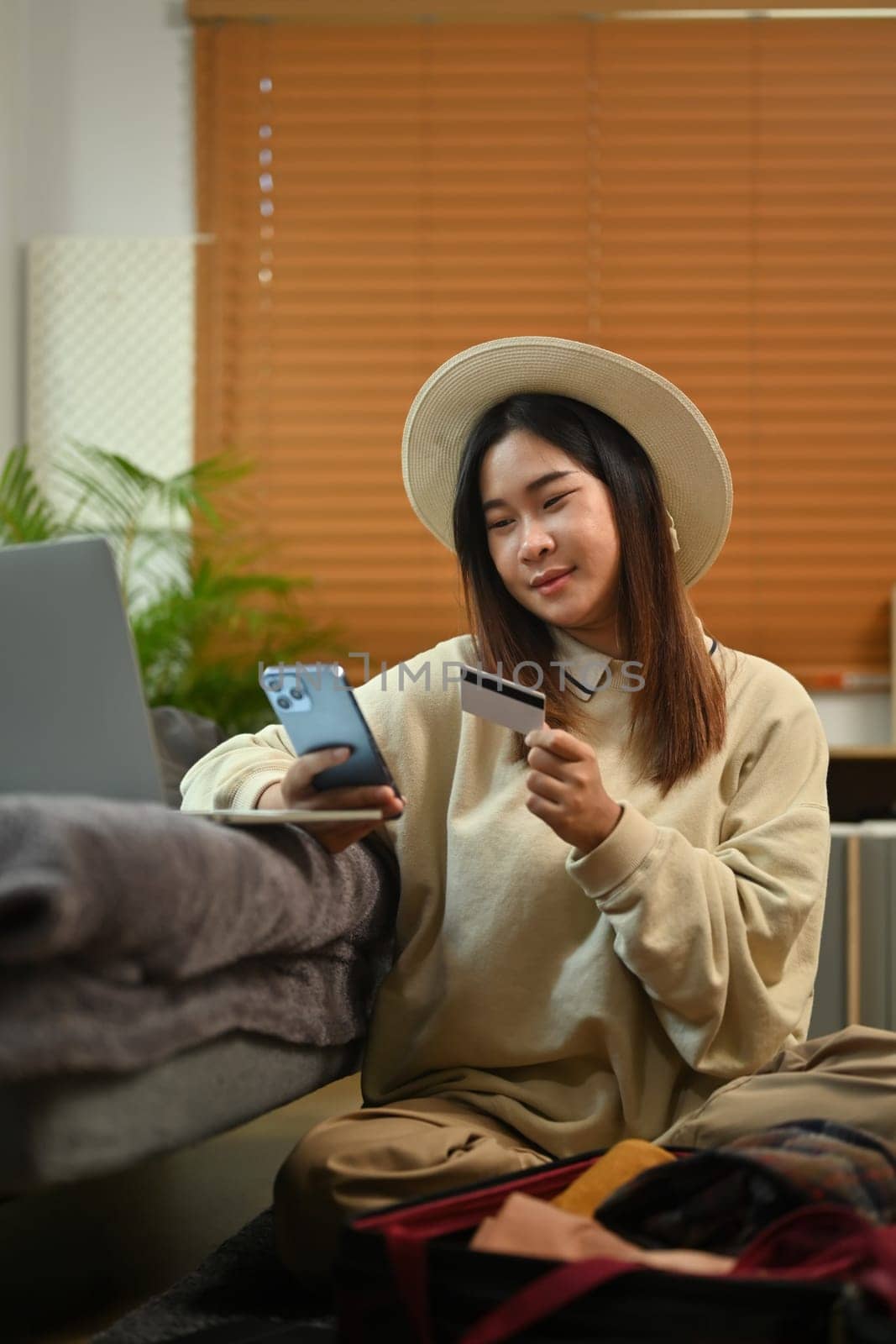 Happy young woman holding credit card and using mobile phone booking tickets or hotel room on web.