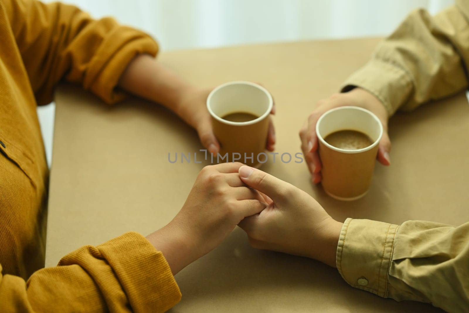 Top view of young lovers having a coffee time while holding hands. Love, relationship and lifestyle concept. by prathanchorruangsak