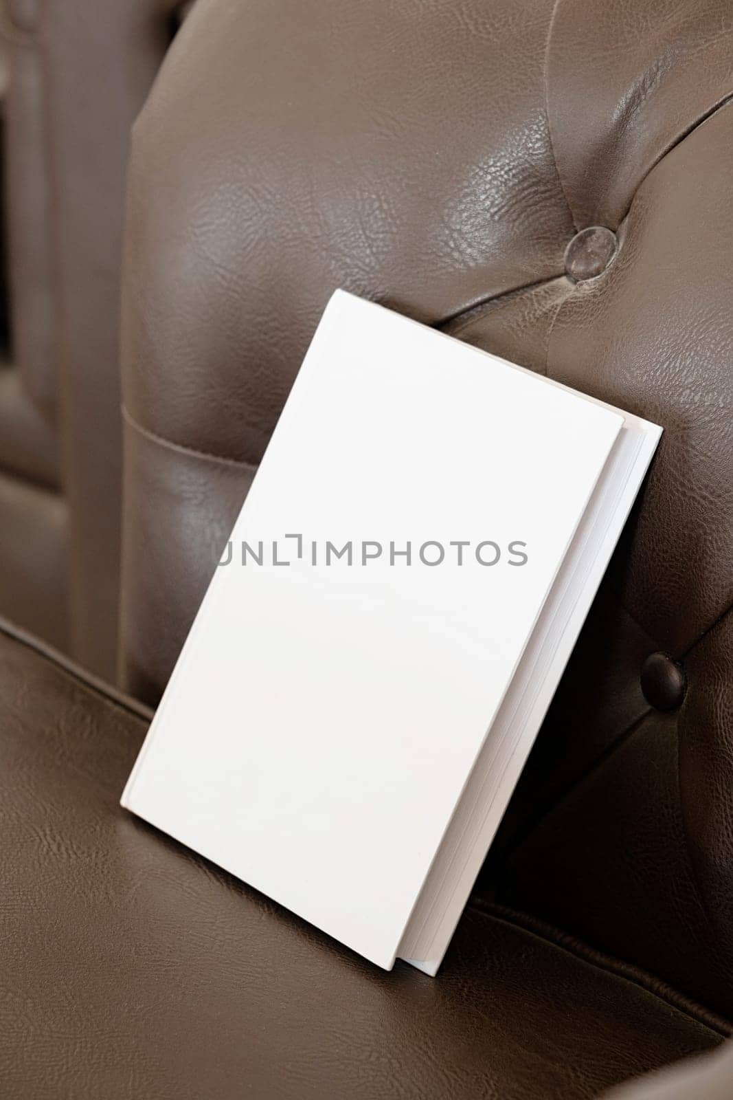 Book with blank cover on brown leather couch