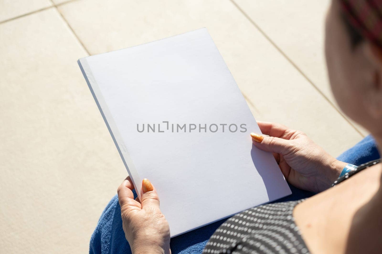 unrecognizable woman holding blank magazine for mockup design, sitting by the swimming pool by Desperada