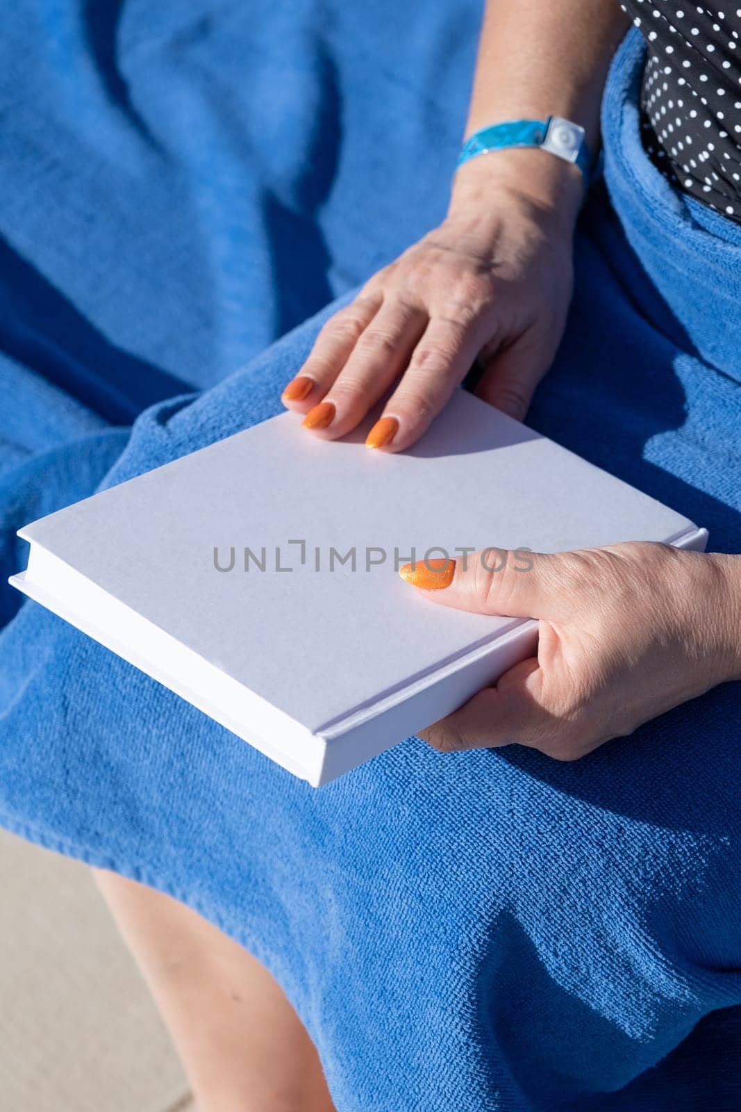 reading at vacation. unrecognizable woman holding blank magazine for mockup design, sitting by the swimming pool in blue towel