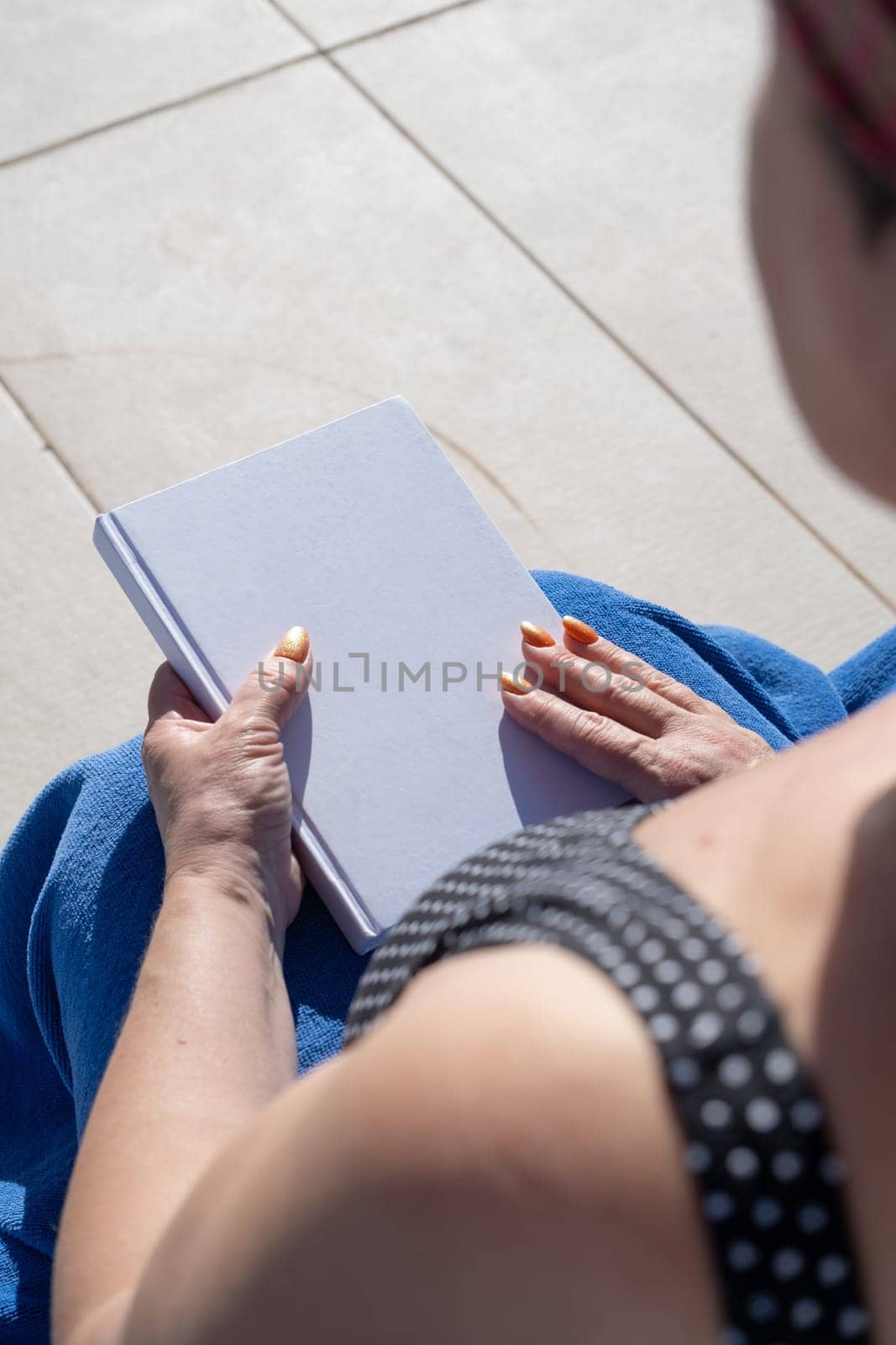 reading at vacation. unrecognizable woman holding blank magazine for mockup design, sitting by the swimming pool in blue towel