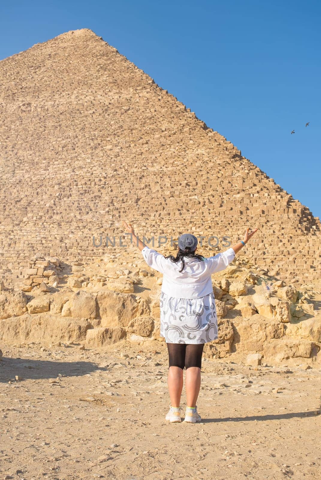 mature adult woman traveler wearing light colour clothing, facing the Pyramids of Gyza