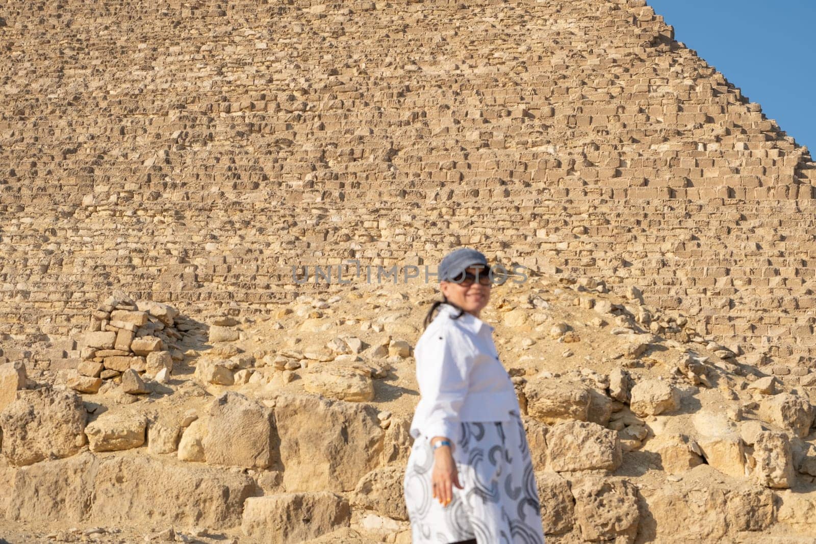 mature adult woman traveler wearing light colour clothing, facing the Pyramids of Gyza