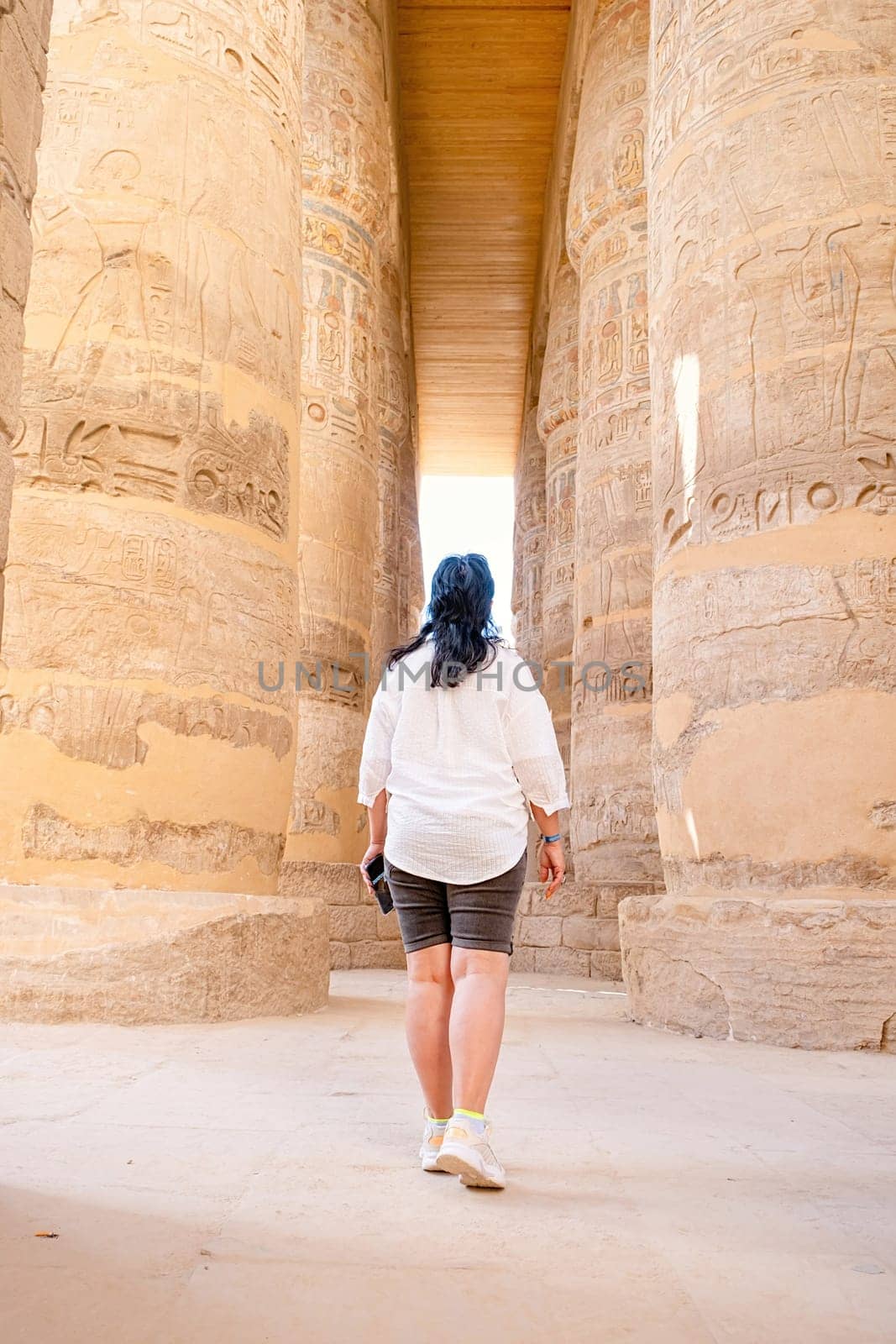 mature adult woman traveler explores the ruins of the ancient Karnak temple in the city of Luxor in Egypt. Great row of columns with carved hieroglyph