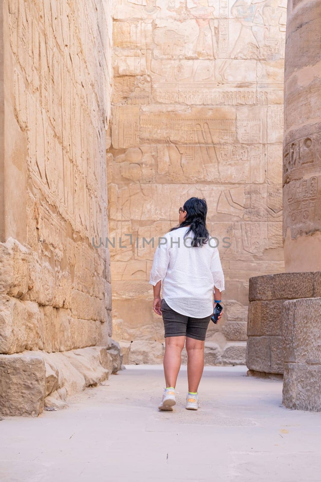 mature adult woman traveler explores the ruins of the ancient Karnak temple in the city of Luxor in Egypt. Great row of columns with carved hieroglyph