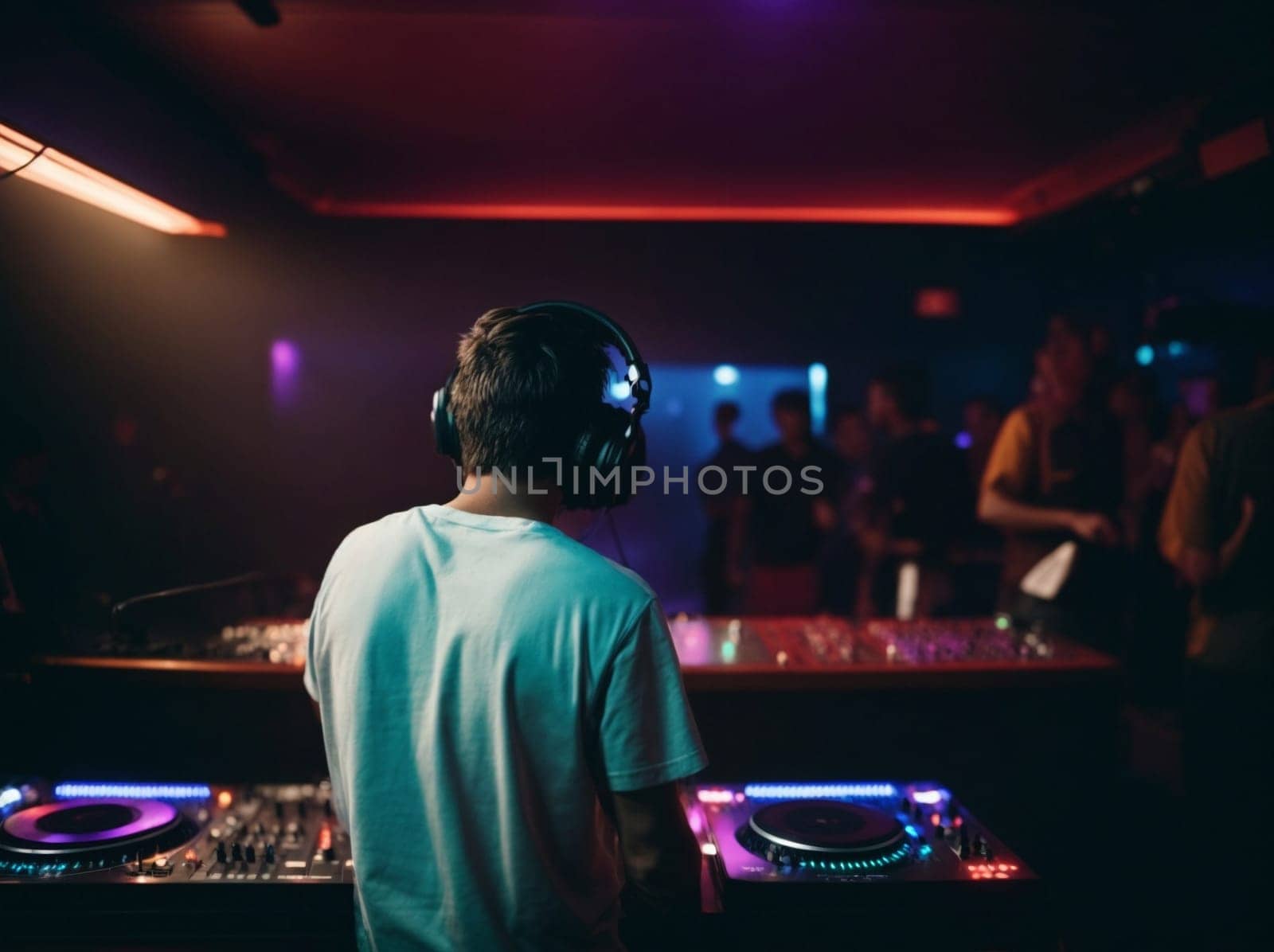 A man in a DJ booth wearing headphones, focused on operating the equipment during a lively music event.