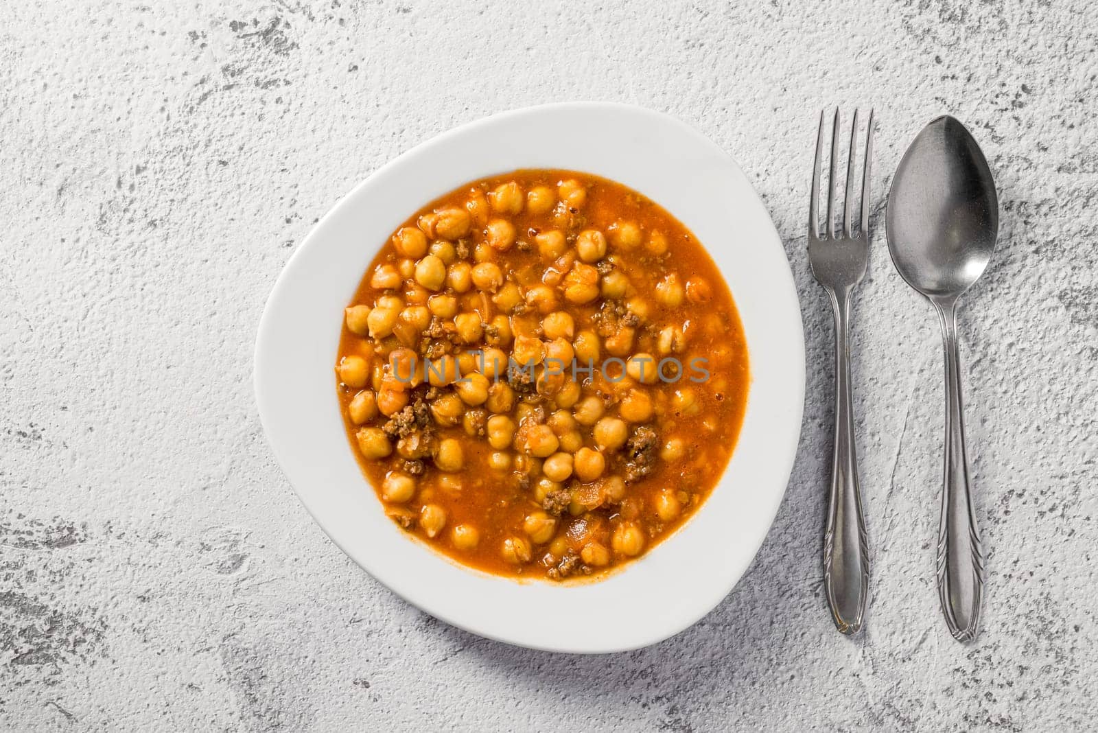 Chickpea stew with minced meat on a white porcelain plate on a stone table