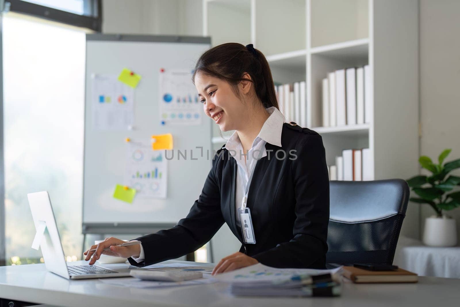 Charming Asian business woman sitting working on laptop in office.