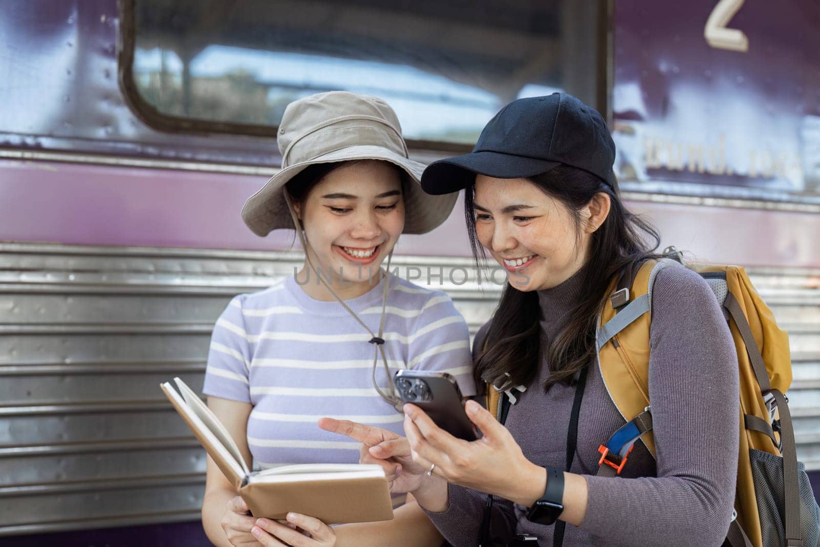 two women traveler friends are at the train station checking the map of the city on mobile by itchaznong