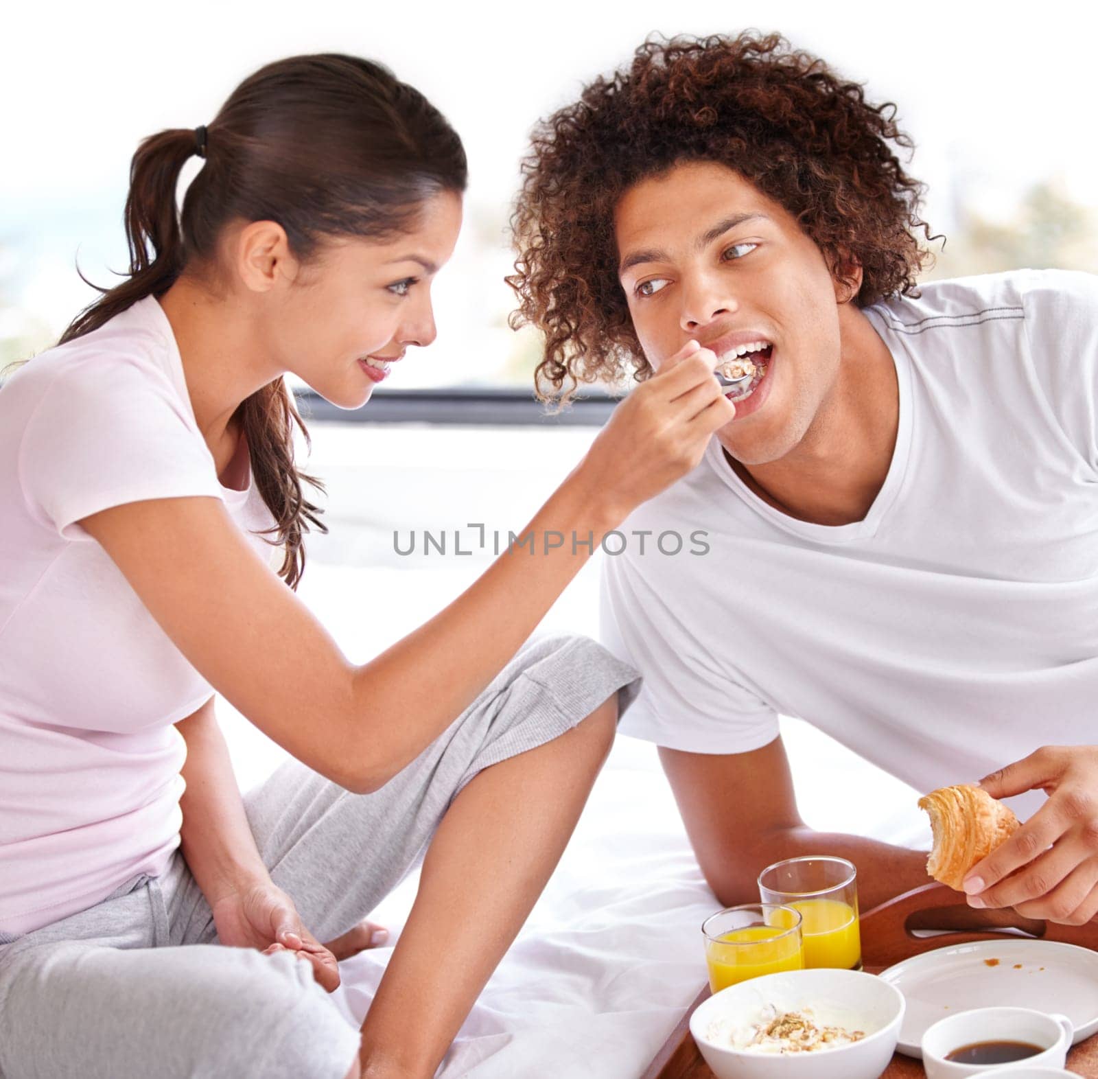 Couple, feeding and breakfast in bed on vacation, healthy meal and celebrating anniversary at home. People, marriage milestone and love or loyalty in relationship, romance and food for nutrition by YuriArcurs