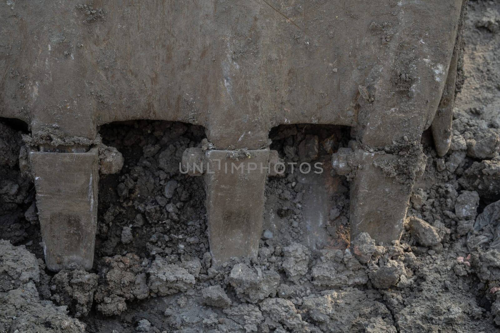 Closeup dirty bucket of backhoe working at construction site. Bucket teeth of backhoe digging soil. Crawler excavator digging on soil. Excavating machine. Earthmoving machine. Excavation vehicle.