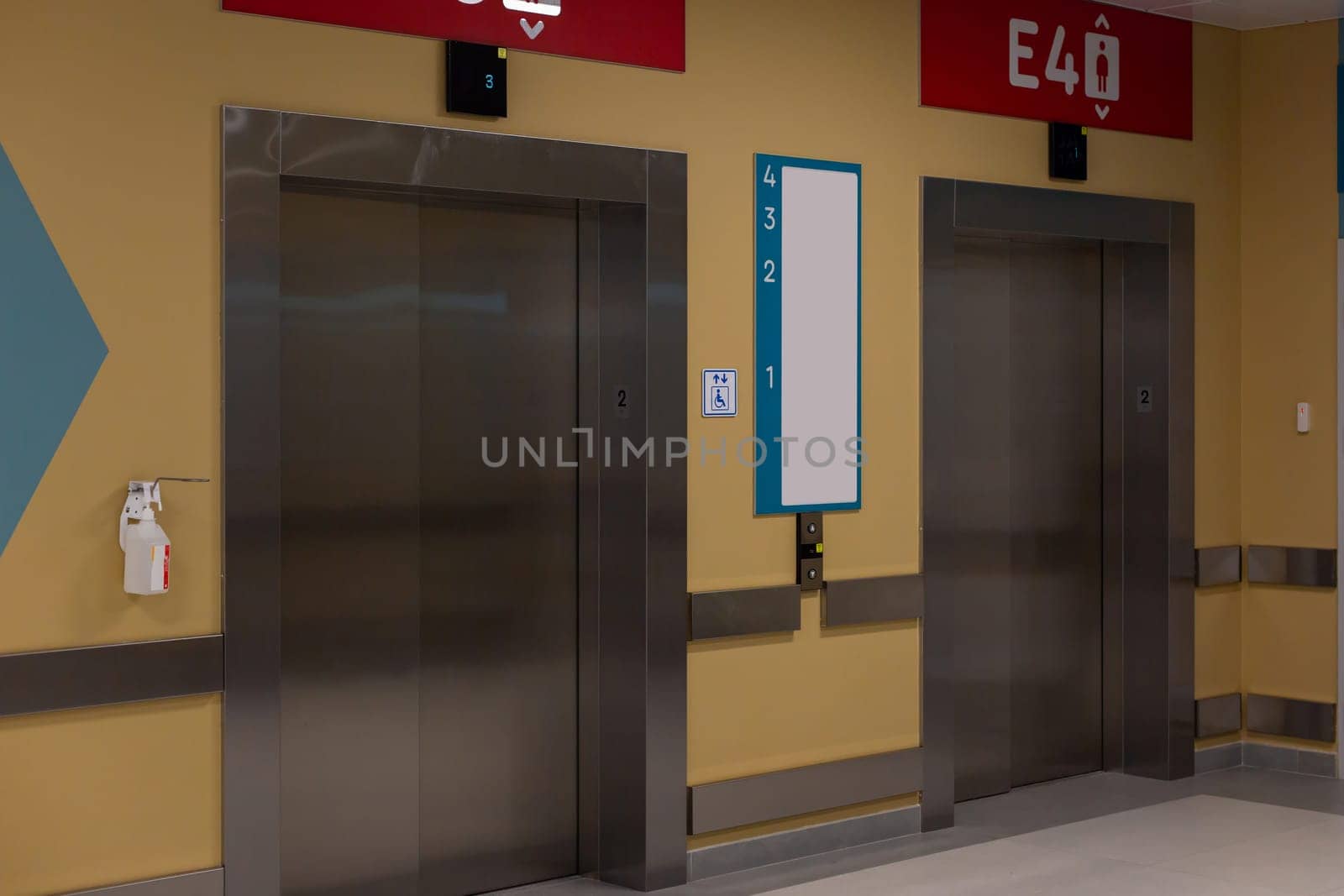 Modern elevator doors with red directional signs in a corridor.
