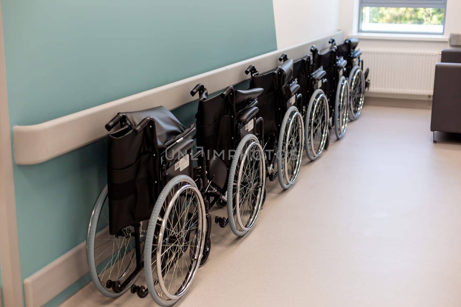 A row of empty folded wheelchairs along a corridor of clinic .