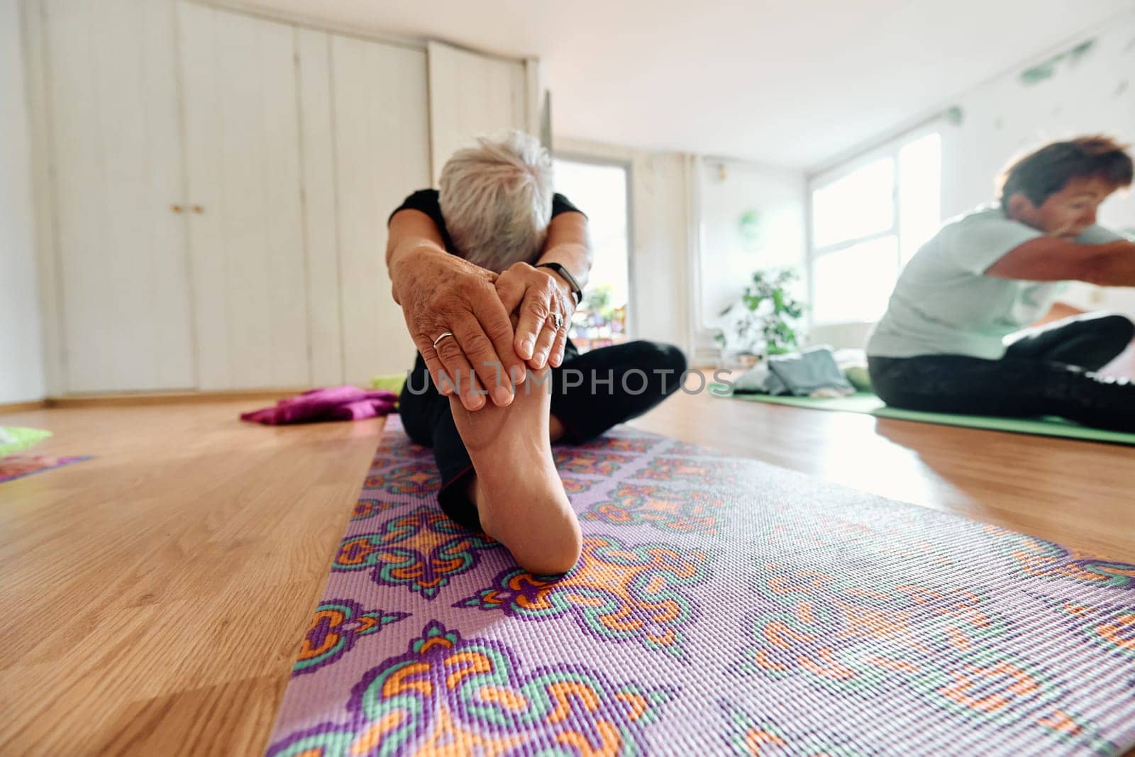 An elderly woman gracefully engages in various yoga poses, stretching her limbs and finding serenity in a modern sunlit space under the guidance of a trained instructor, embodying the essence of active and mindful aging by dotshock