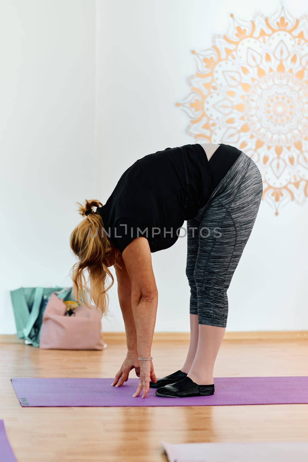 In a sunlit space, a senior woman gracefully practices rejuvenating yoga, focusing on neck, back, and leg stretches, embodying serenity and well-being.
