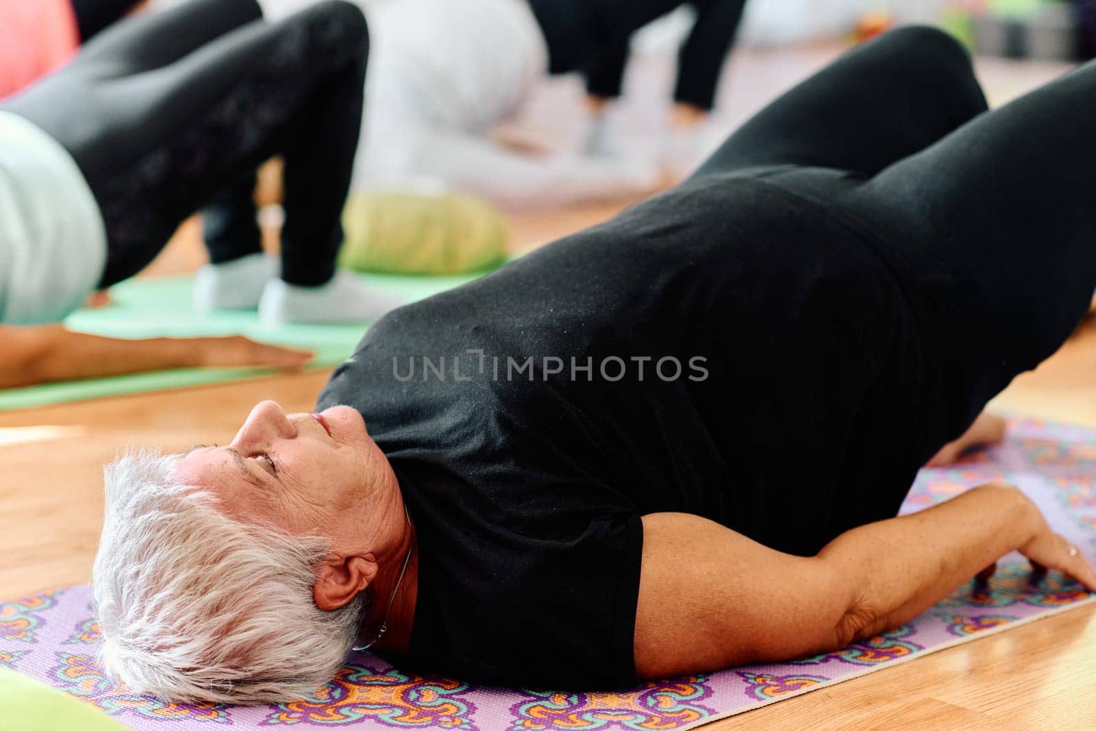 In a sunlit space, a senior woman gracefully practices rejuvenating yoga, focusing on neck, back, and leg stretches, embodying serenity and well-being by dotshock