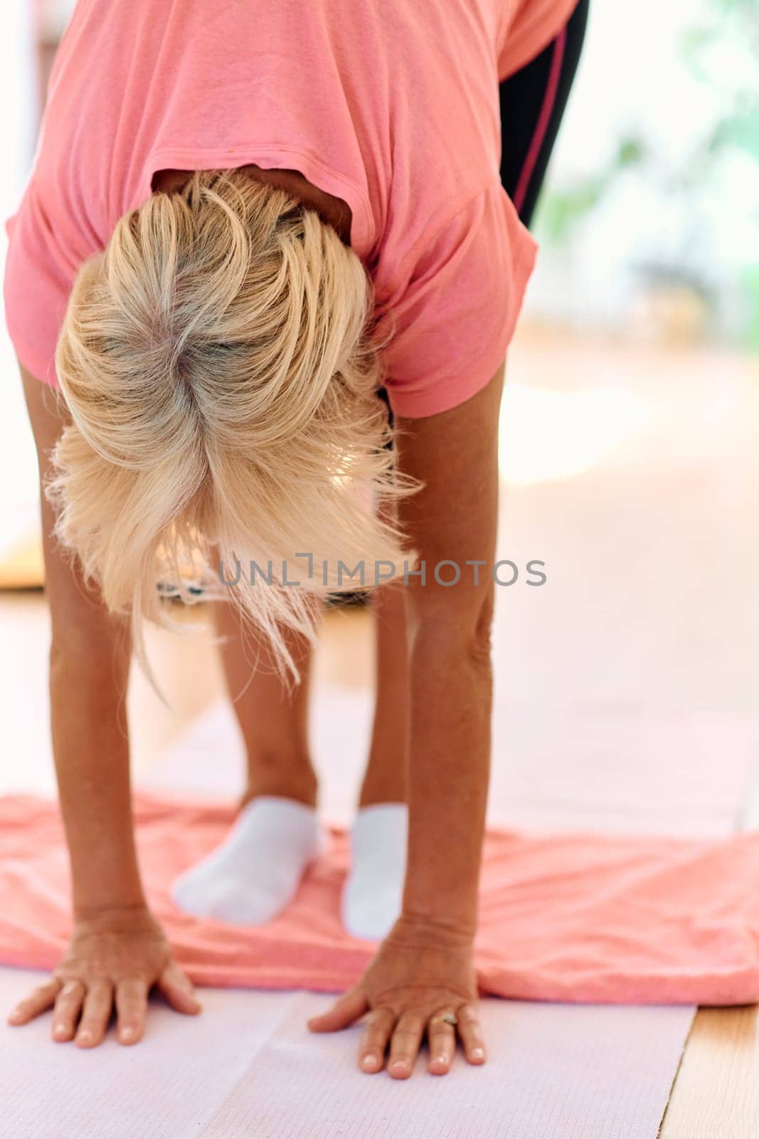 In a sunlit space, a senior woman gracefully practices rejuvenating yoga, focusing on neck, back, and leg stretches, embodying serenity and well-being by dotshock