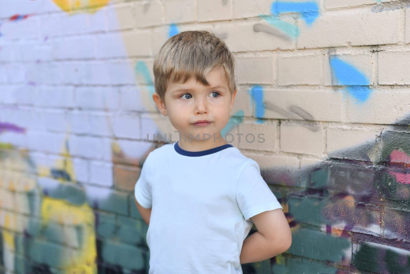 A boy with blue eyes near a colorful wall by Godi