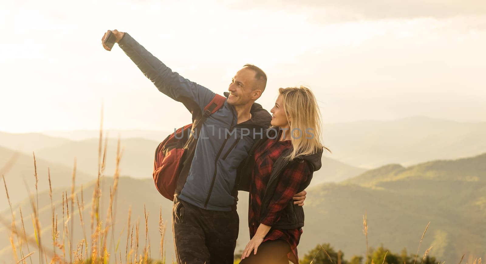 A man and a woman in tourist equipment are standing on a rock and admiring the panoramic view. A couple in love on a rock admires the beautiful views. A couple in love is traveling. A couple on a hike by Andelov13
