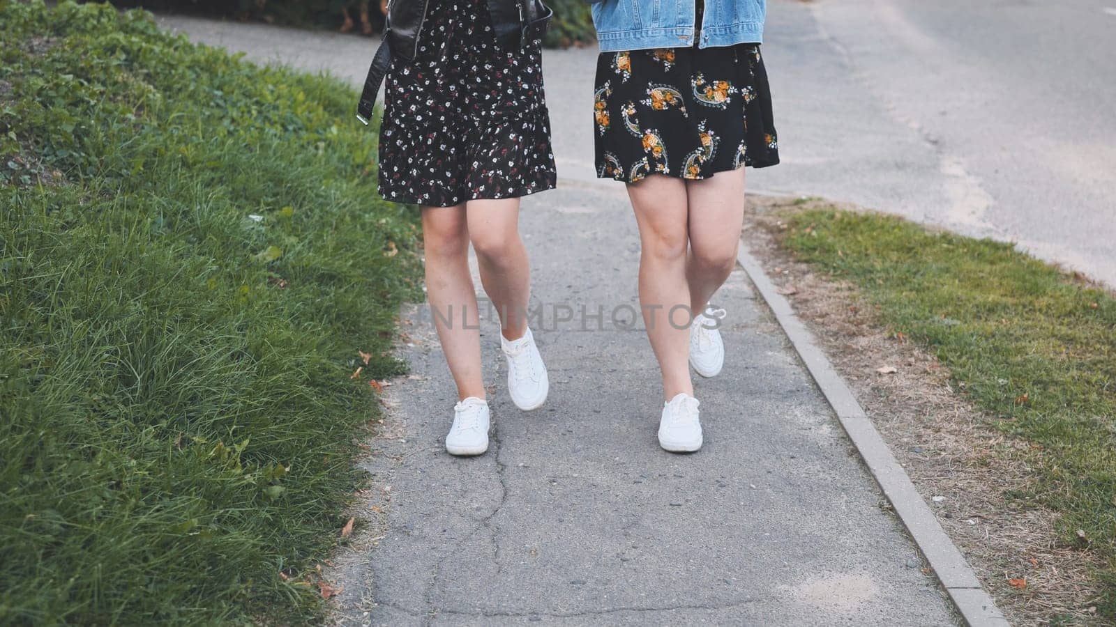 Two girlfriends in white sneakers walk down the street. by DovidPro