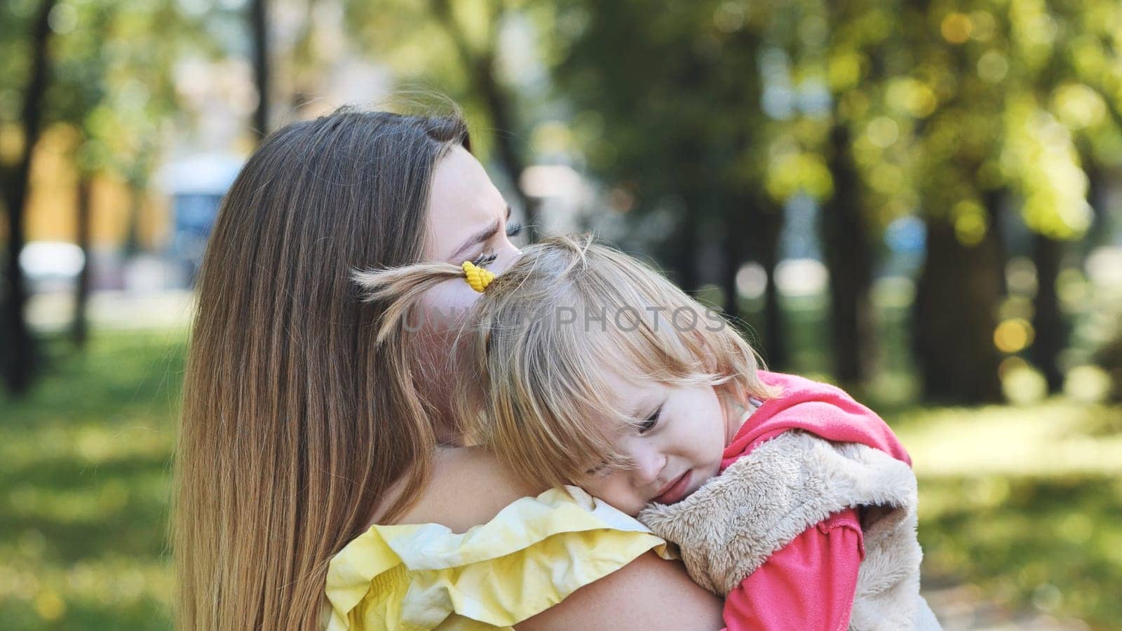 A mother hugs her young daughter in the park in the summer