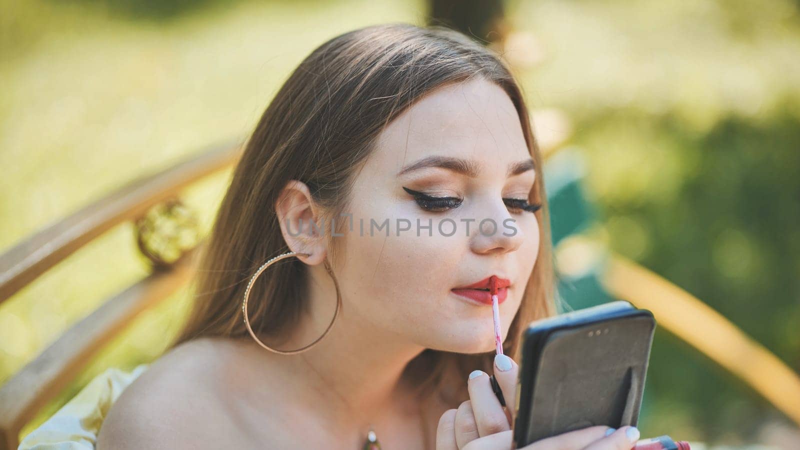 A girl paints her lips in the park in the summer