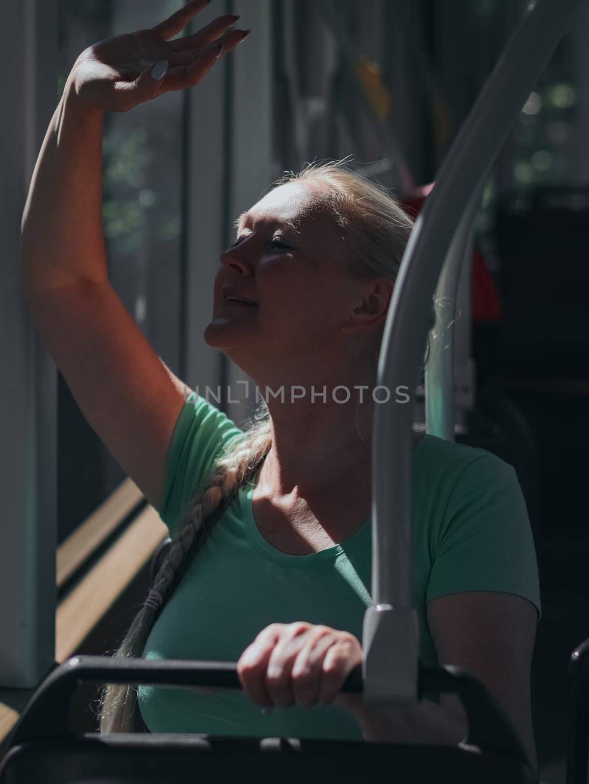 A young beautiful Caucasian blonde woman with a braided braid and a joyful smile sits on a bench in a tram and joyfully waves her hand out the window, close-up side view.