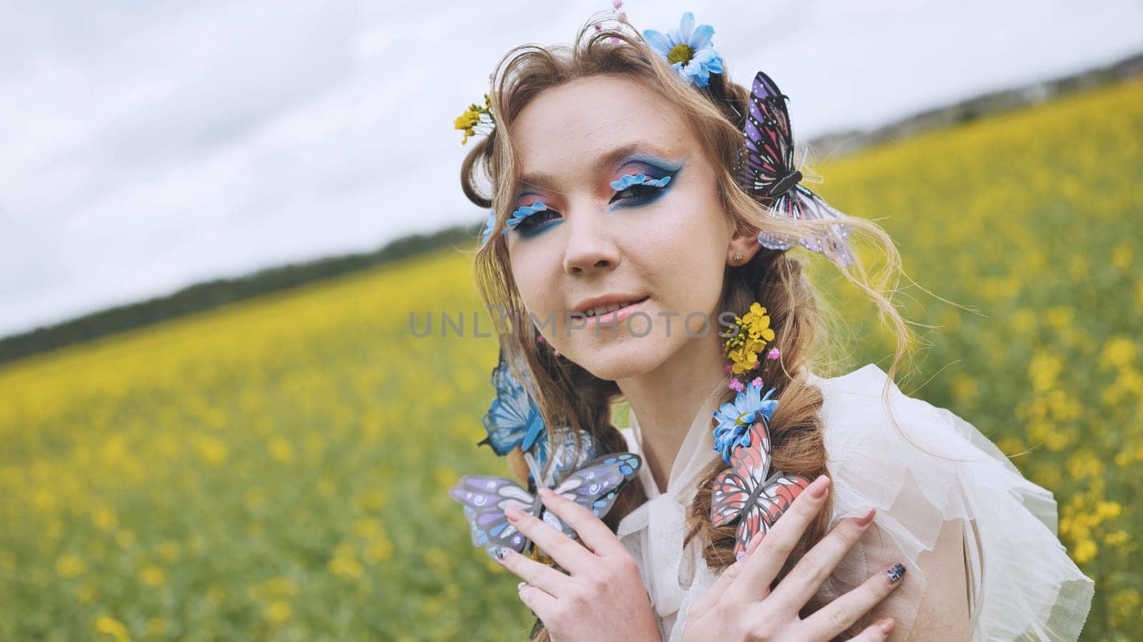 A young girl poses in a rapeseed field with a beautiful hairdo of flowers and butterflies