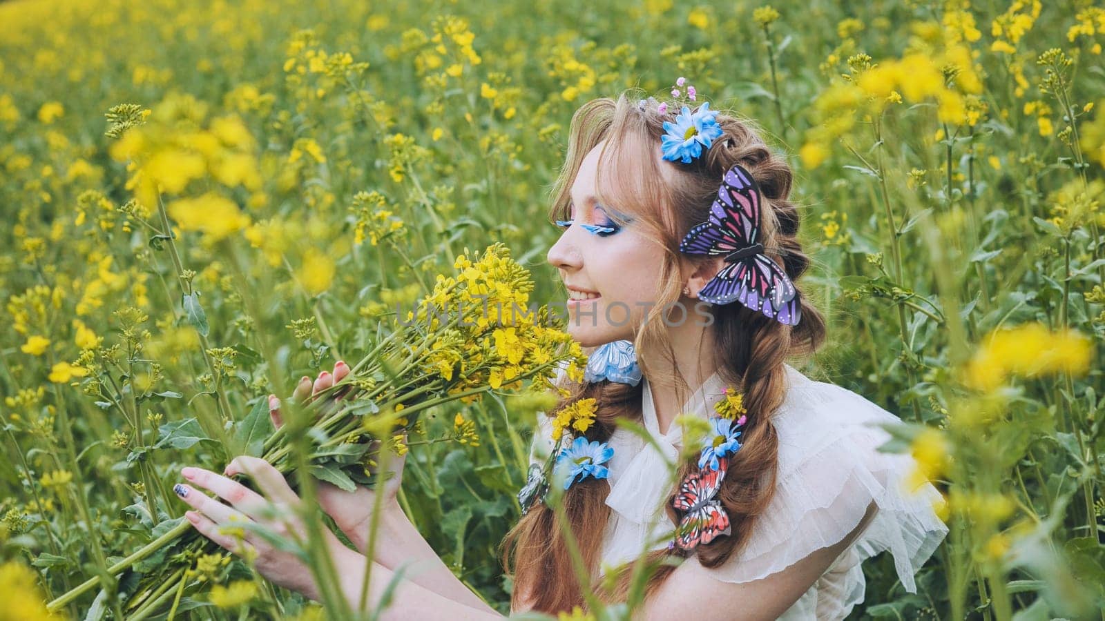 A young girl poses in a rapeseed field with a beautiful hairdo of flowers and butterflies